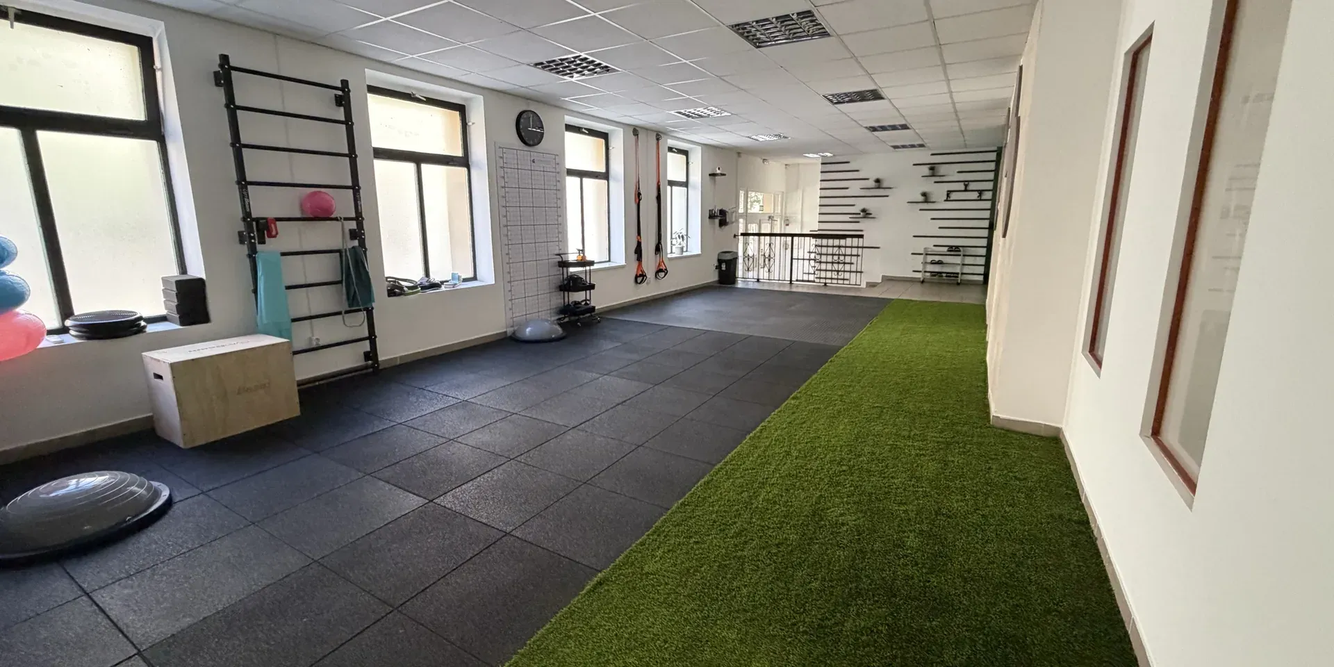 The training area of the Movement Club: wall bars, dumbbells, an artificial turf lane and large windows